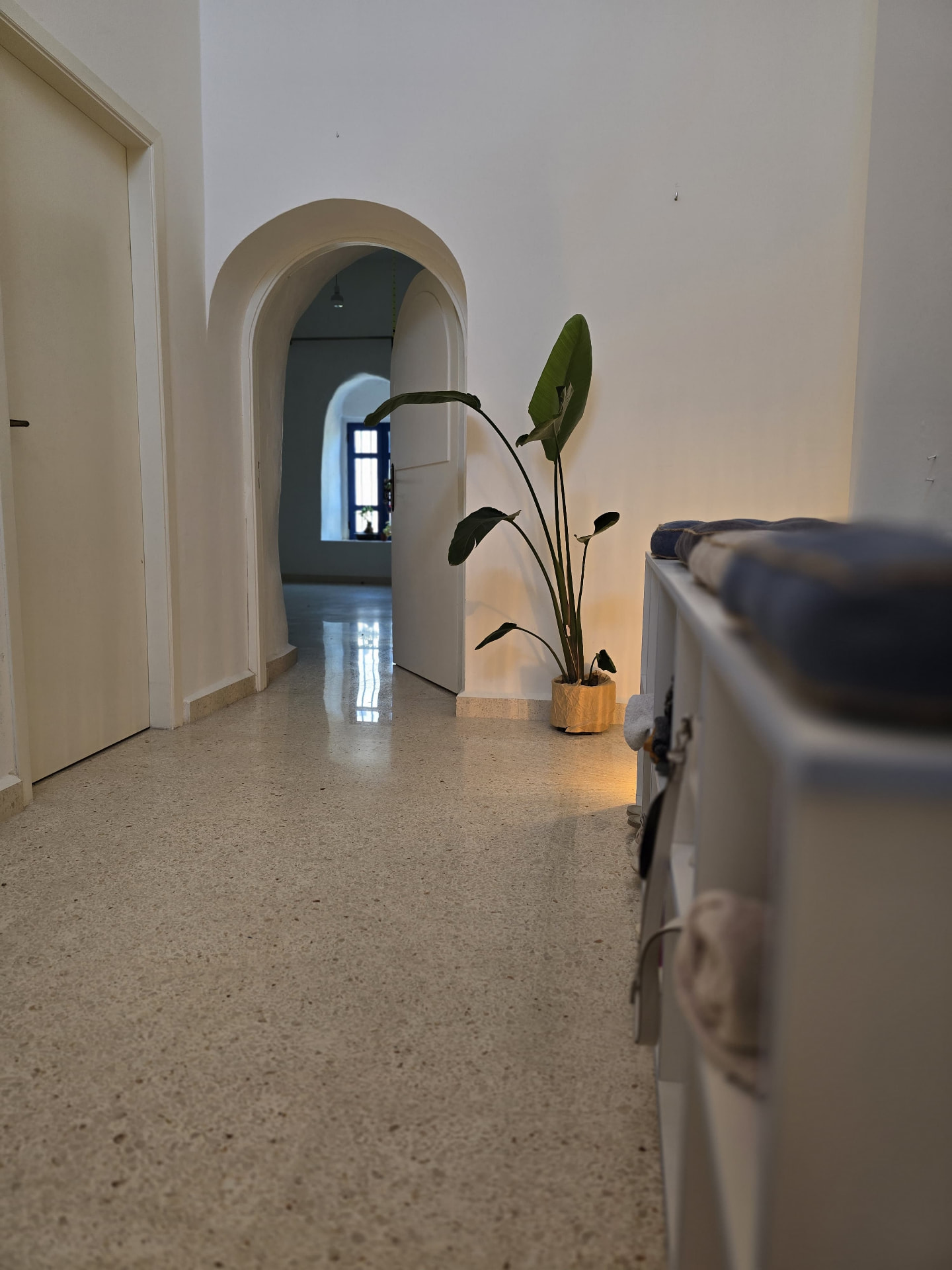Arched hallway leading into the Batroun studio with a plant and cushioned bench