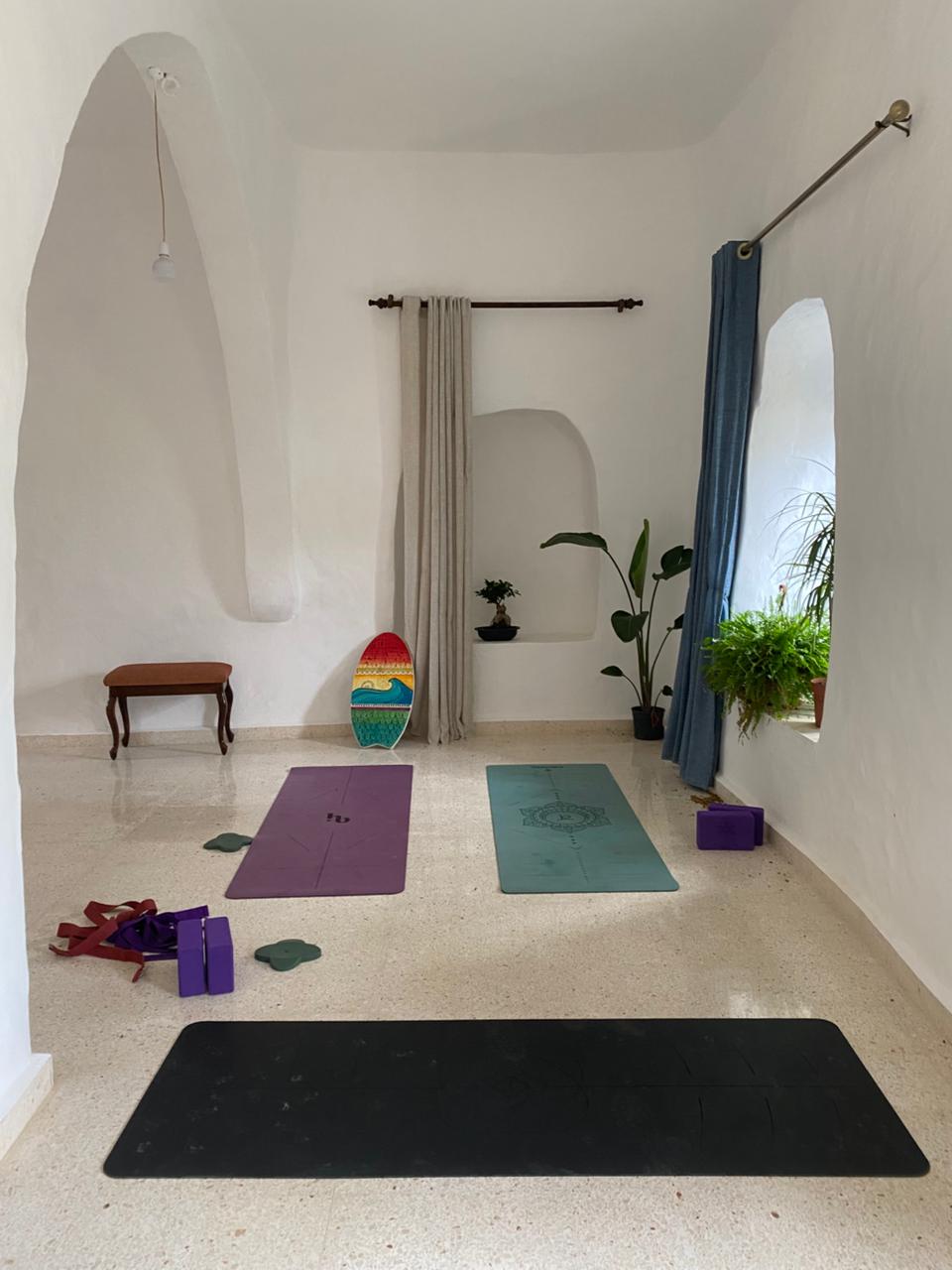 Three yoga mats and blocks set out in the whitewashed arched practice room with plants by the window
