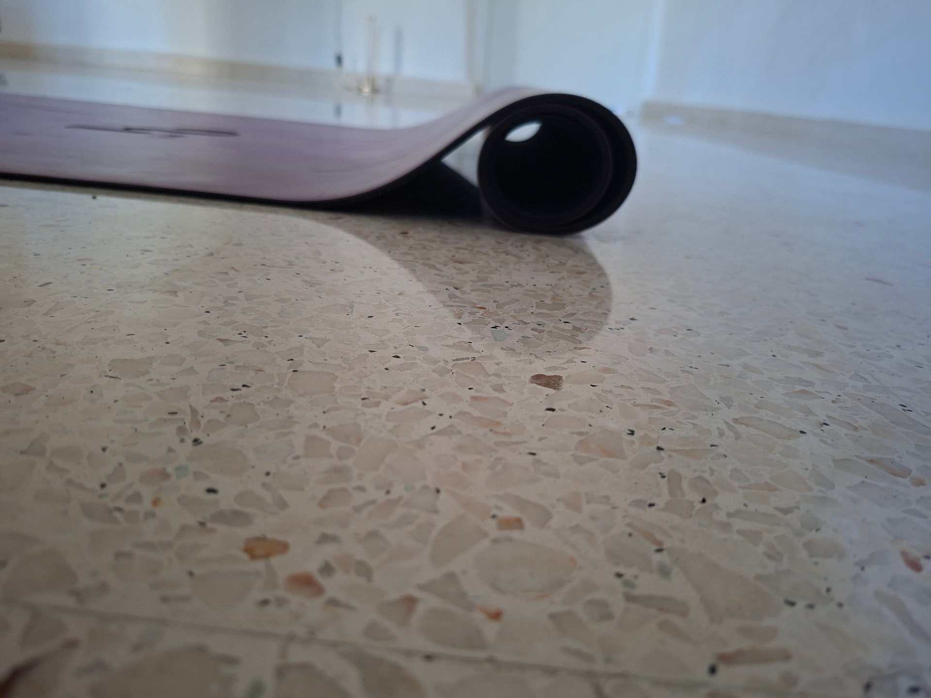 Close view of a rolled blush yoga mat resting on the polished terrazzo studio floor